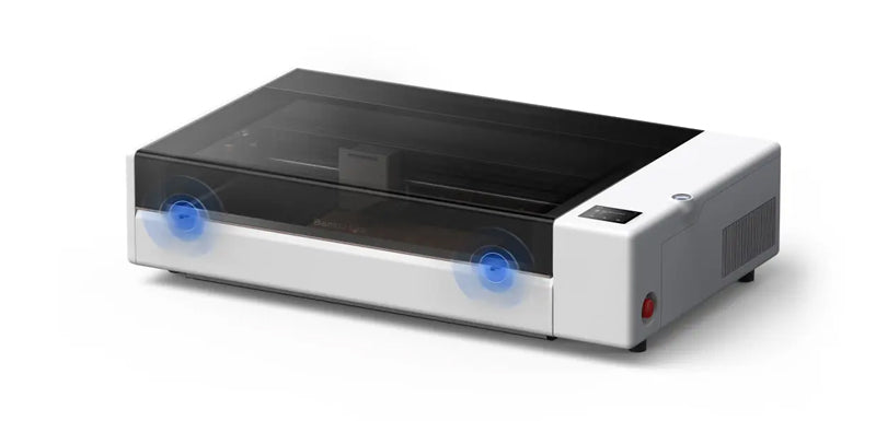A desktop laser engraver machine with a white and black body, featuring a transparent top cover, blue circular graphic overlays indicating laser points, and a small red power button on the side, set against a plain white background.